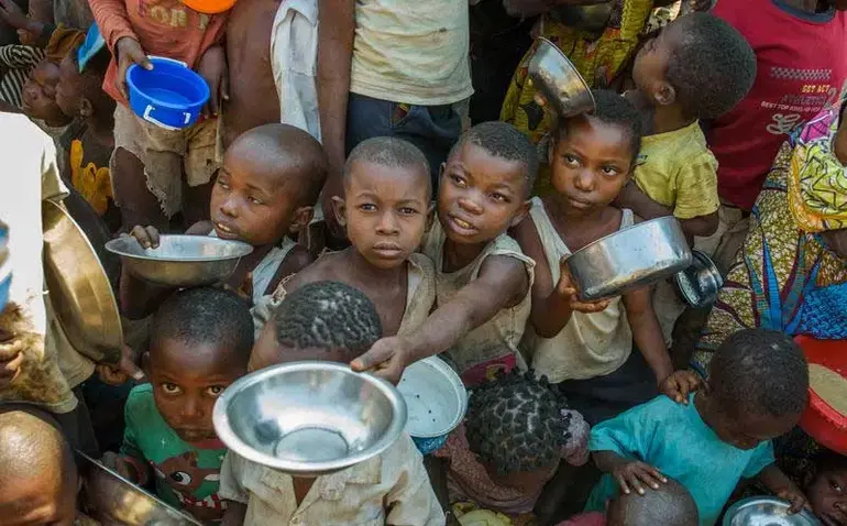 A group of vulnerable Nigerian children holding empty bowls, illustrating the severe economic hardship and poverty rate in the country.