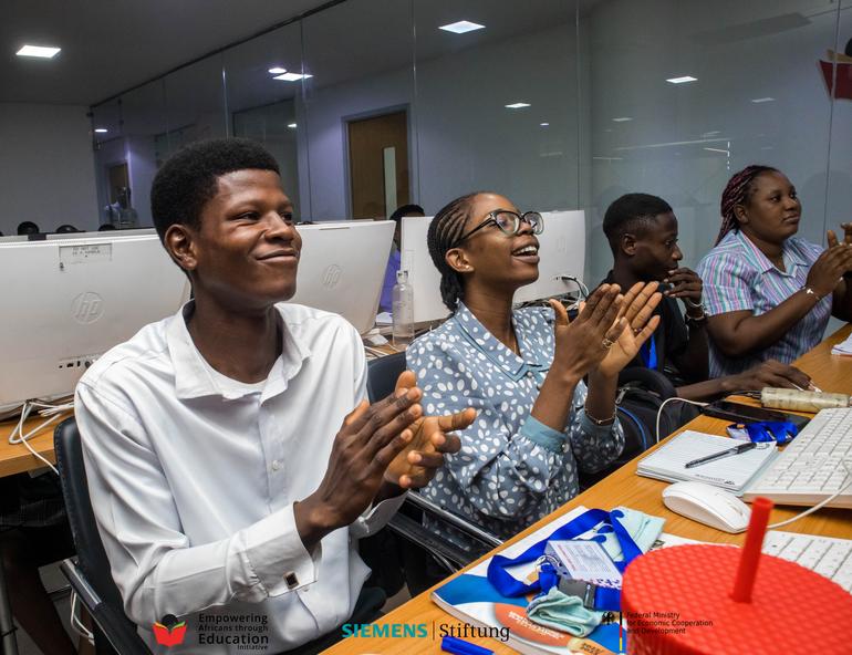 Excited Nigerian tech students smiling and applauding in a computer lab classroom during a career mentorship session.
