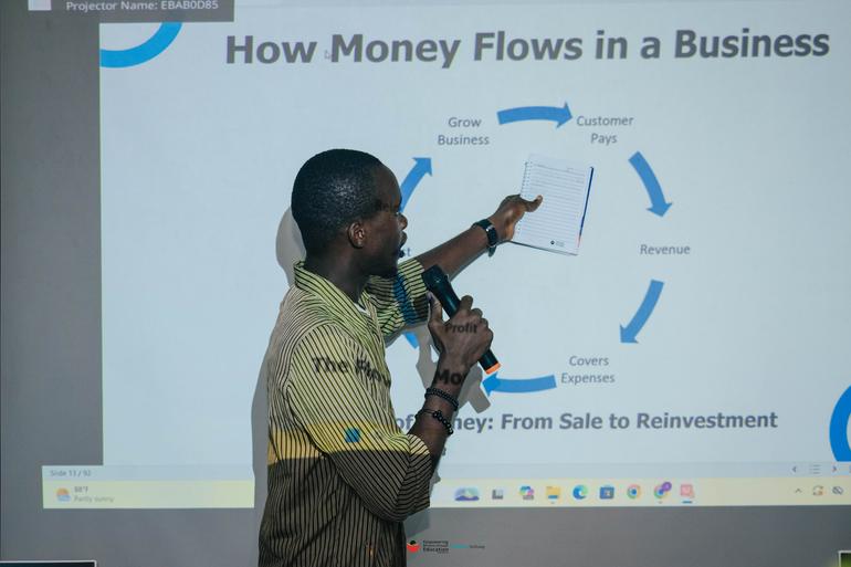 A male instructor presenting a slide on how money flows in a business during a career readiness and entrepreneurship module.