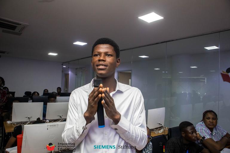 A confident young Nigerian male participant speaking into a microphone during a BeMINT soft skills and communication workshop.