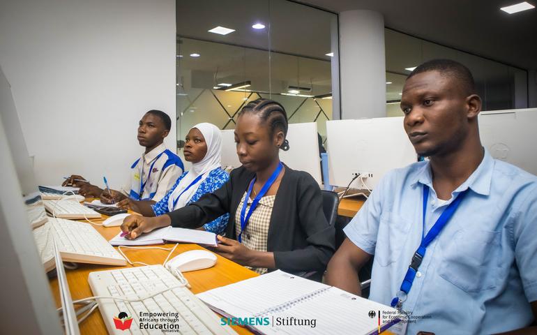 Four young Nigerian students diligently taking notes and working on desktop computers during a free 6-week intensive training programme.