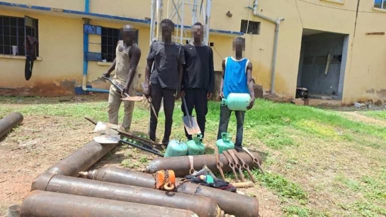 Paraded suspects standing behind recovered NNPCL pipes, gas cylinders, and diggers in Adamawa State.
