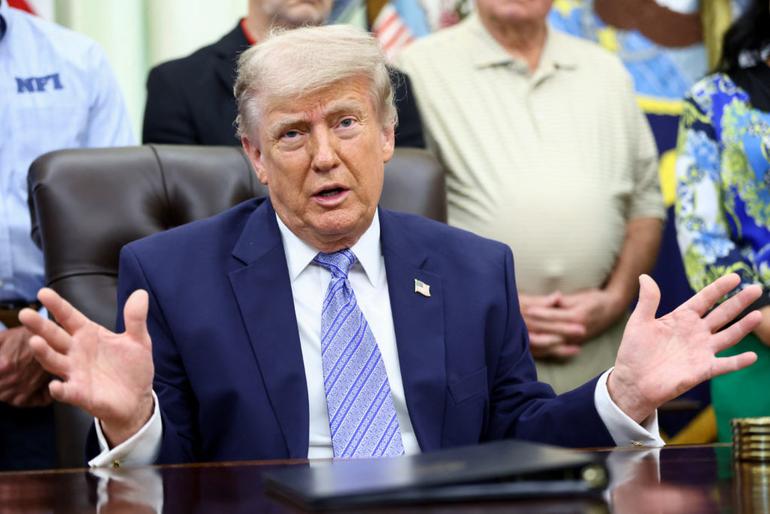 President Donald Trump sitting at a desk, gesturing with both hands during an immigration policy briefing.