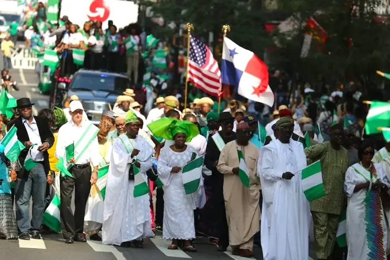 A crowd of Nigerian-Americans and green card seekers marching in a parade while waving Nigerian and American flags.