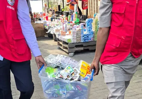 NAFDAC officials carrying a plastic crate filled with confiscated sachet alcohol during an enforcement raid.
