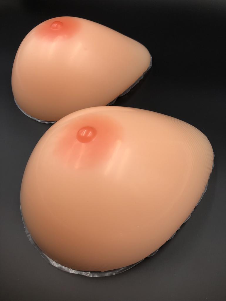 A pair of realistic flesh-toned silicone breast prostheses with teardrop shapes sitting on a plain black surface.