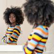A young Black woman with an afro hairstyle standing with folded arms and looking thoughtfully at her reflection in a mirror.