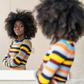 A young Black woman with an afro hairstyle standing with folded arms and looking thoughtfully at her reflection in a mirror.