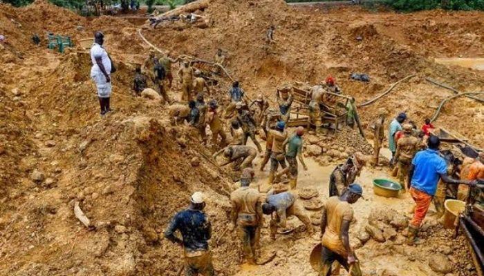 A crowded, muddy informal and artisanal gold mining site in Nigeria with workers using manual tools.