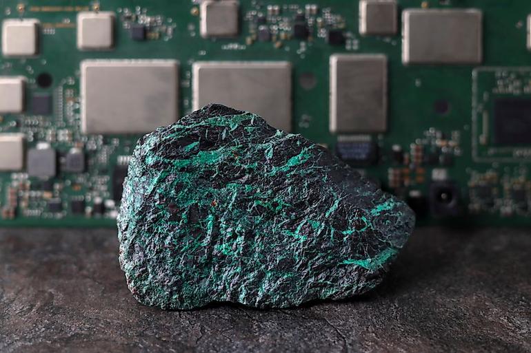 A rare earth element ore sample containing green mineral veins placed in front of an electronic computer circuit board.