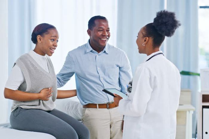 Medical doctor in a white lab coat explaining kidney transplant surgery to a concerned couple in a Nigerian clinic.