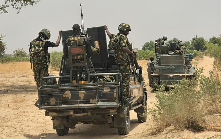 A Nigerian military gun truck and a tracked armored vehicle patrolling a dirt road in a rural combat zone in Borno State.
