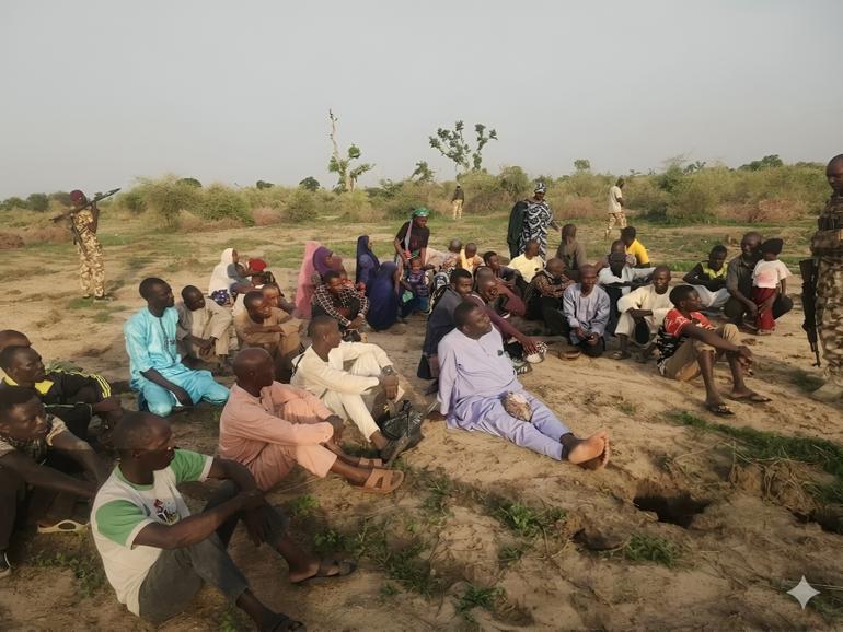 Rescued civilians sitting in an open field in Borno State after Nigerian Army troops dismantled a JAS/ISWAP roadblock.