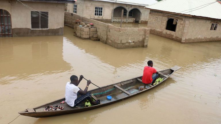 Aerial view of two men paddling a canoe through a heavily flooded residential neighbourhood in Lagos where water levels have reached building windows.