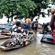 Commuters, including a woman with a child, using a canoe to bypass a submerged minivan on a flooded road in Owode-Elede, Lagos.