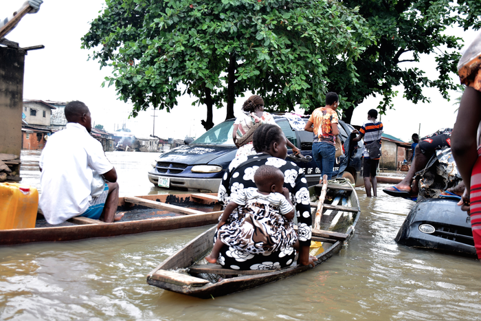 Commuters, including a woman with a child, using a canoe to bypass a submerged minivan on a flooded road in Owode-Elede, Lagos.