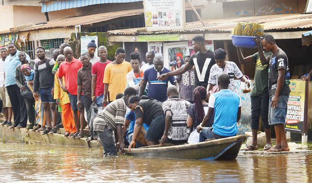 A long queue of Lagos residents waiting to board a wooden canoe to navigate a flooded street in Warewa during the 2026 rainy season.