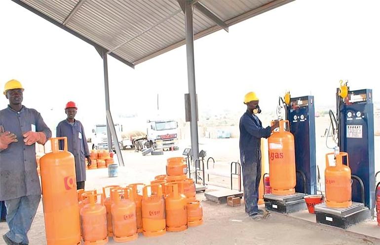 Plant attendants filling bright orange cooking gas cylinders for retail distribution at a standard local LPG dispensing hub.