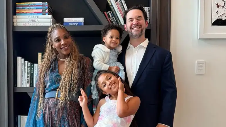 Alexis Ohanian with wife Serena Williams and their two daughters posing together in front of a bookshelf.