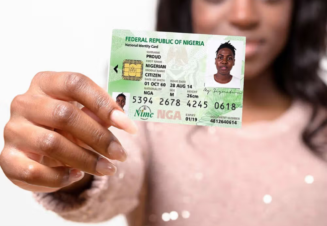 A close-up of a Nigerian citizen holding up the official green and white Federal Republic of Nigeria National Identity Card.