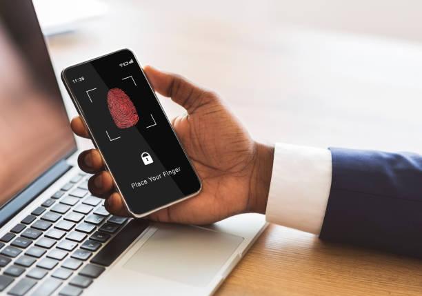A professional holding a smartphone displaying a secure biometric fingerprint scanning interface next to a laptop keyboard.