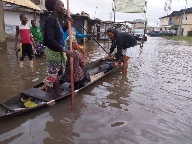 Residents using a wooden canoe to navigate a completely flooded residential street in Lekki Lagos.