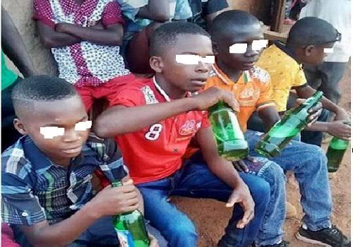Young underage boys sitting outdoors drinking alcoholic beverages from green glass bottles in Nigeria.