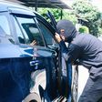 A photo of a masked man trying to enter into a car