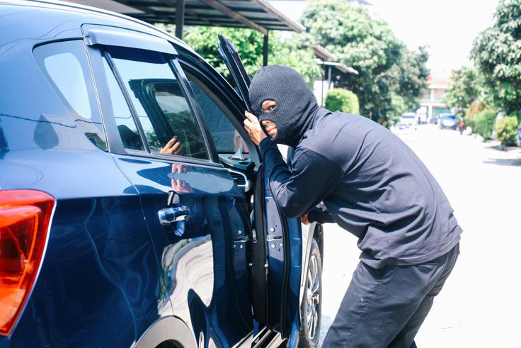 A photo of a masked man trying to enter into a car