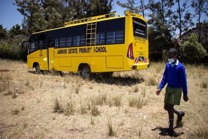 A masked pupil from Jamhuri Estate Primary School in Kibra Constituency walks past their school bus (Image: Files)