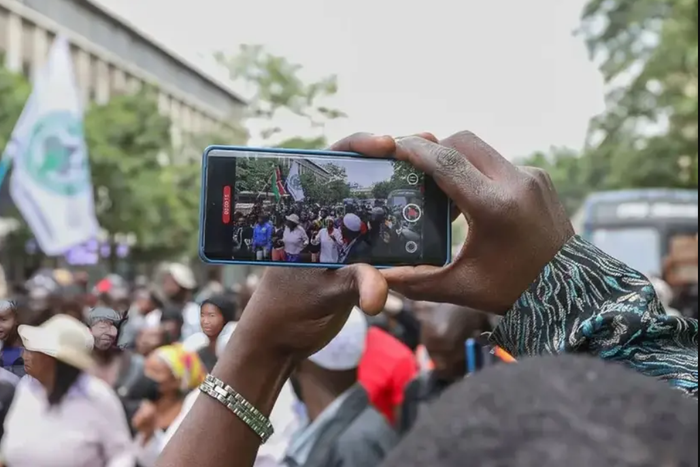 A photo of a person recording a video of people protesting