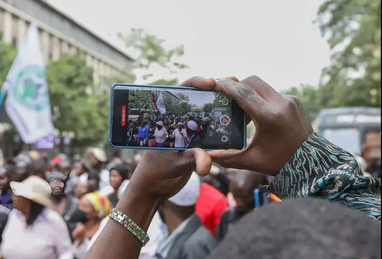 A photo of a person recording a video of people protesting