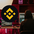 Man wearing hoodie and using computers and an inset of Binance logo