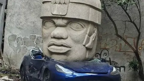 En CDMX aparece Tesla aplastado por una cabeza Olmeca