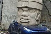 En CDMX aparece Tesla aplastado por una cabeza Olmeca