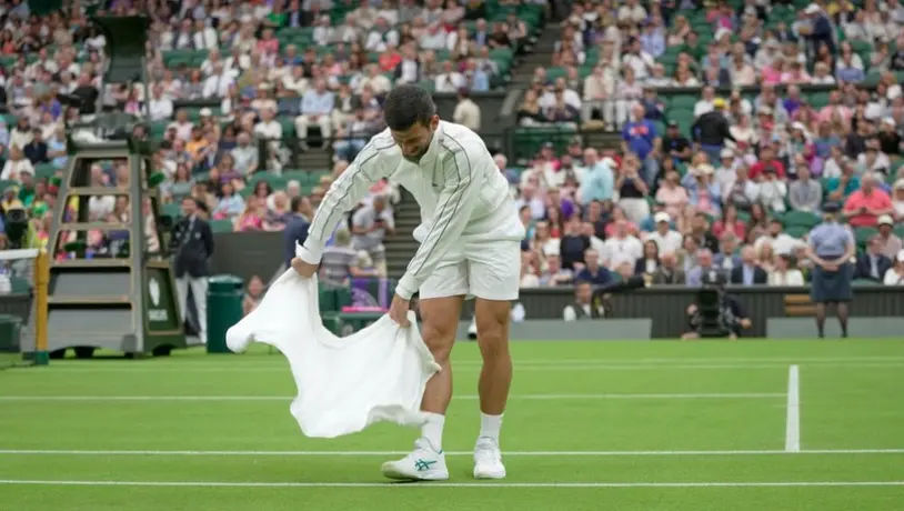 Novak Djokovic utiliza su toalla para secar la cancha en Wimbledon