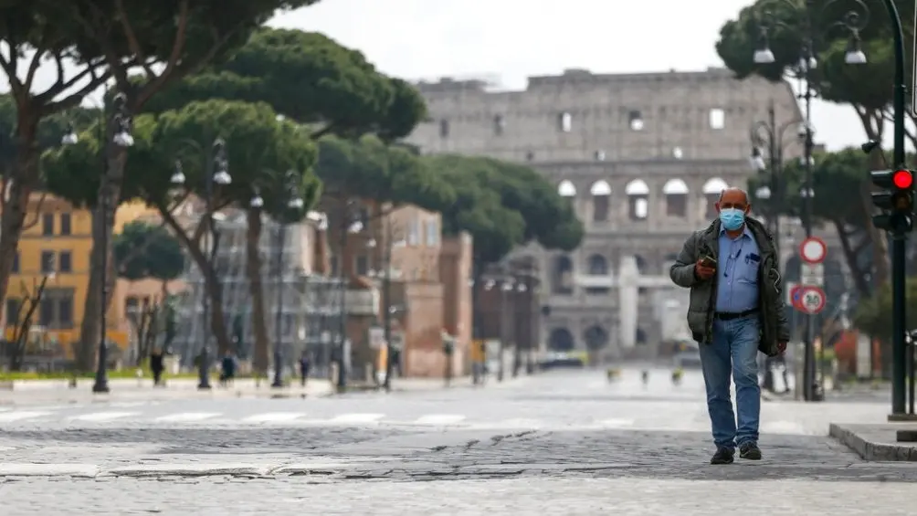 Hombre camina en una calle solitaria que da al Coliseo romano | AP