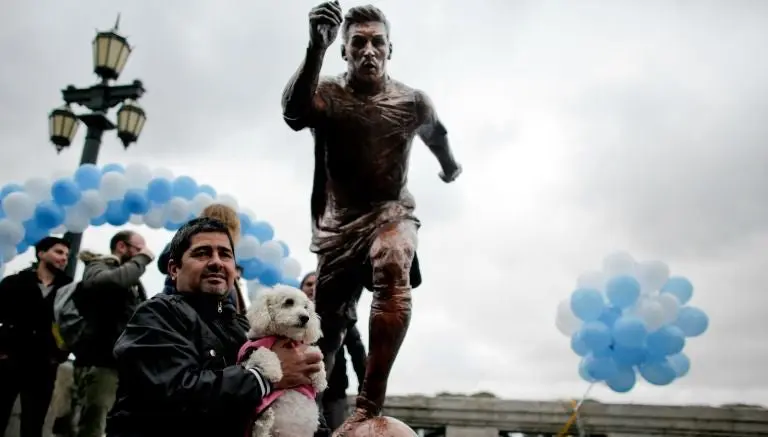 Aficionado argentino posa junto a la estatua de Lionel Messi | AP