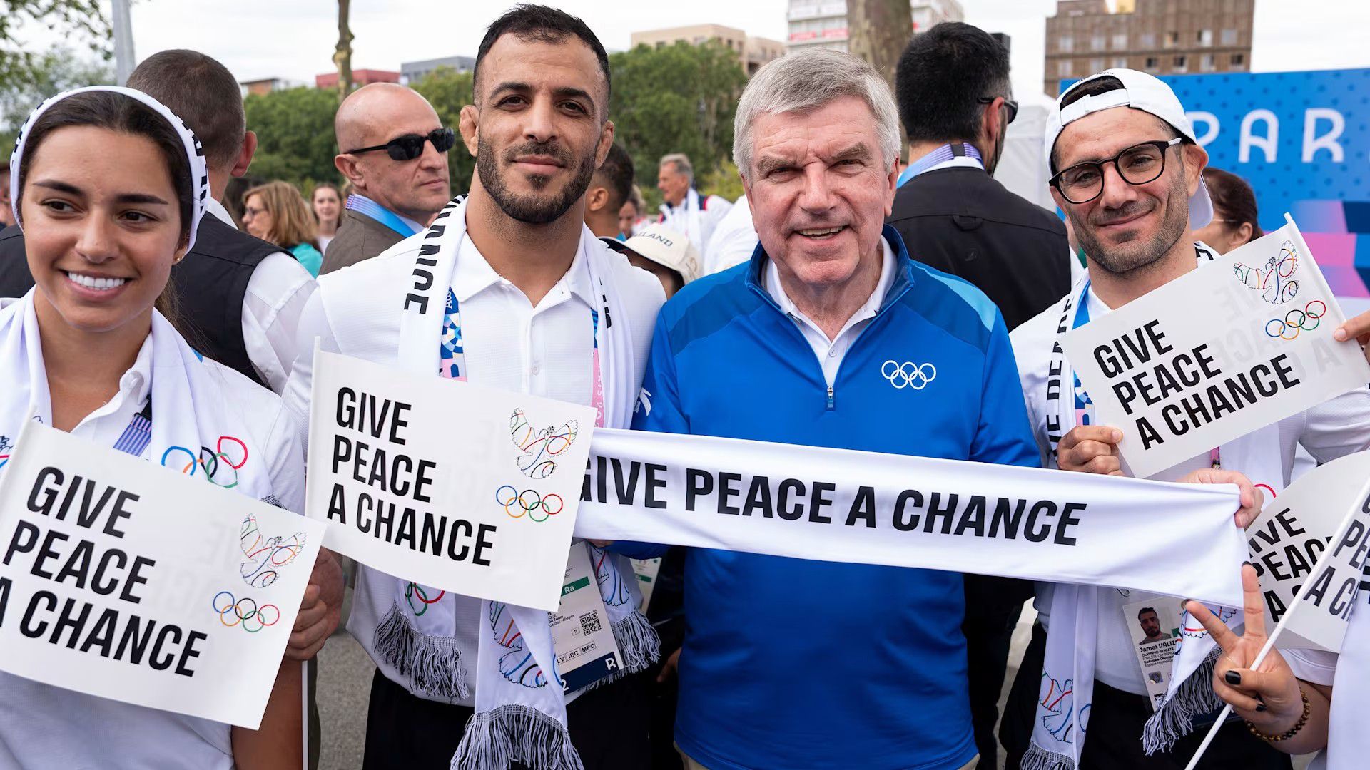 Sálakkal, zászlócskákkal és fotókkal harcol a békéért a Nemzetközi Olimpiai Bizottság elnöke